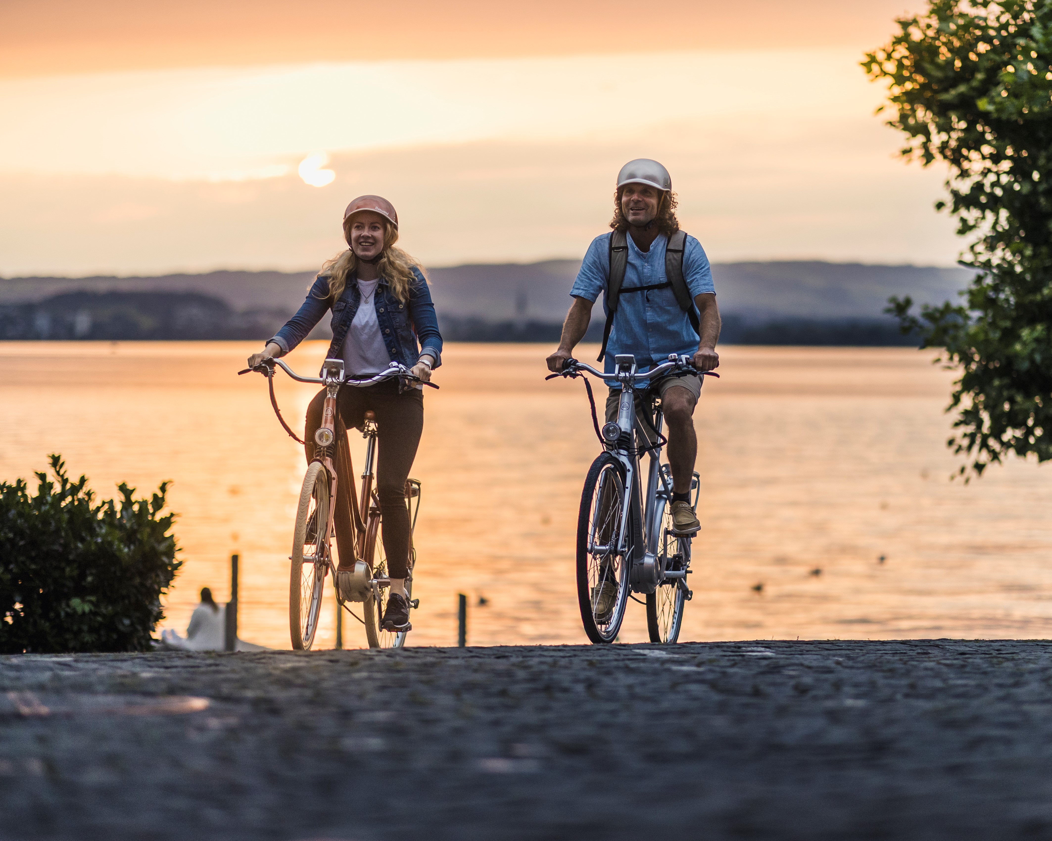Zwei Velofahrer mit See im Hintergrund in Abendstimmung