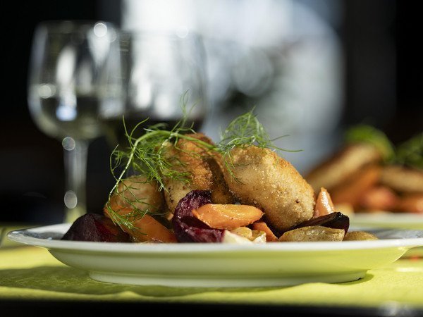Cordon bleu plate with various vegetables and wine glass in the background
