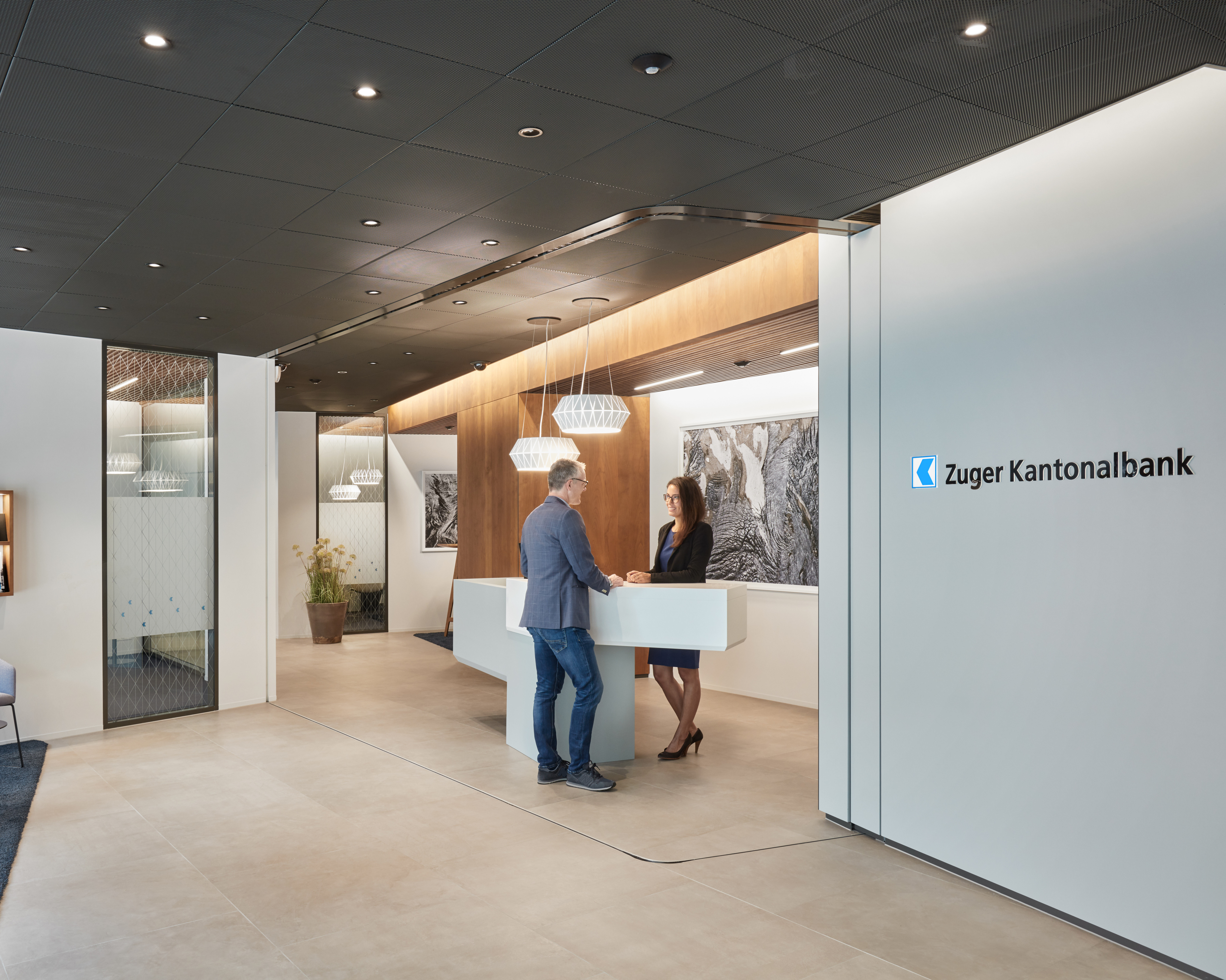 Mann steht bei Frau am Tresen in einer Filiale der Zuger Kantonalbank